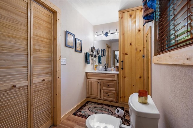 bathroom featuring vanity, wood finished floors, baseboards, a closet, and toilet