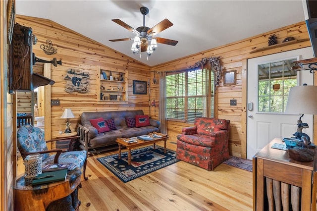 living area featuring wooden walls, ceiling fan, lofted ceiling, and wood finished floors