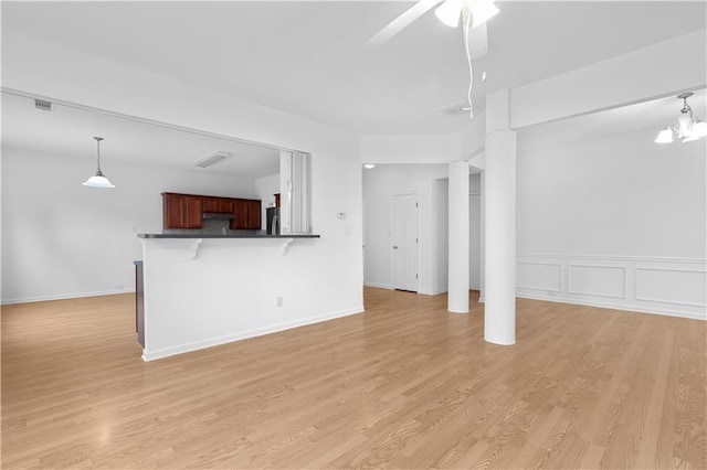 unfurnished living room with ceiling fan with notable chandelier and light hardwood / wood-style floors