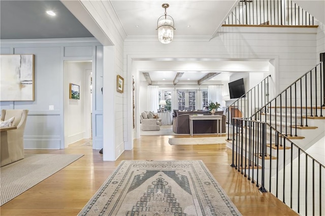 foyer entrance featuring beamed ceiling, a notable chandelier, light hardwood / wood-style floors, and ornamental molding