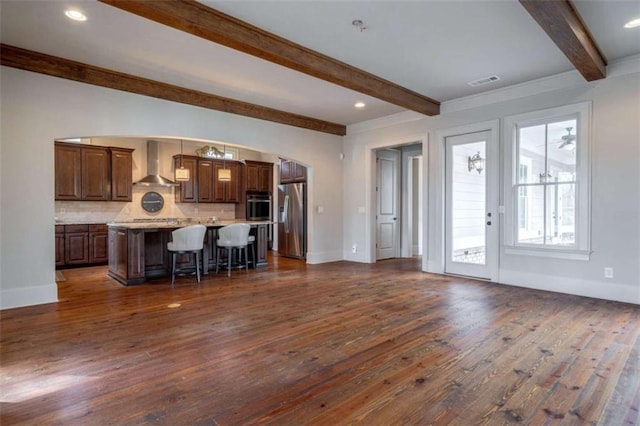 kitchen featuring stainless steel refrigerator with ice dispenser, a breakfast bar area, a kitchen island, beam ceiling, and wall chimney range hood