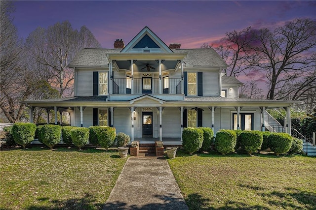 victorian home featuring a ceiling fan, covered porch, a balcony, and a front lawn