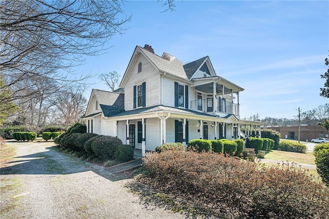 view of front of house featuring covered porch, driveway, roof with shingles, and a balcony