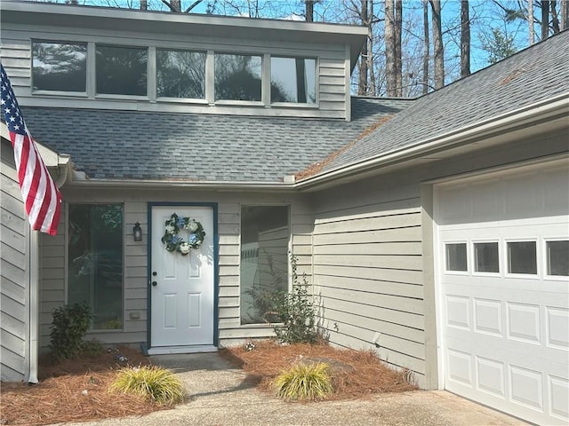 property entrance with an attached garage and a shingled roof