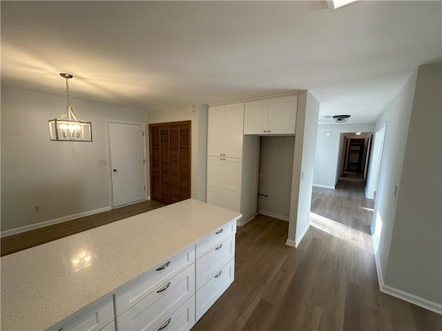 kitchen featuring baseboards, light stone counters, hanging light fixtures, white cabinetry, and dark wood-style flooring