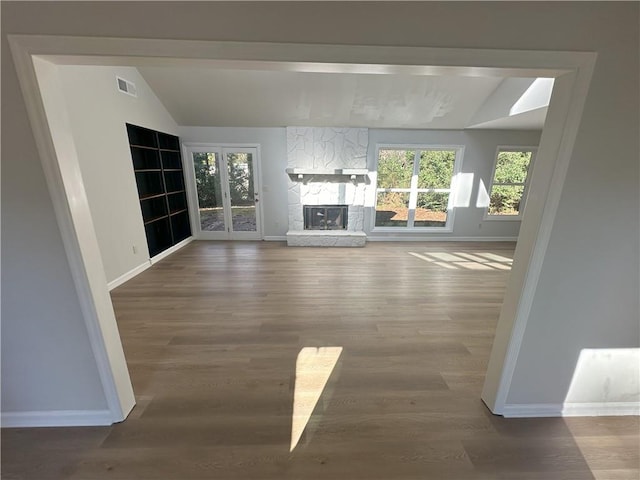 unfurnished living room with visible vents, baseboards, vaulted ceiling, a stone fireplace, and wood finished floors