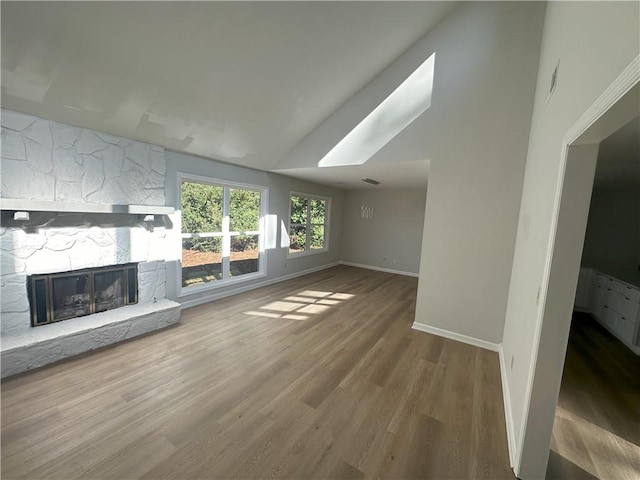 unfurnished living room with a stone fireplace, lofted ceiling, wood finished floors, and baseboards