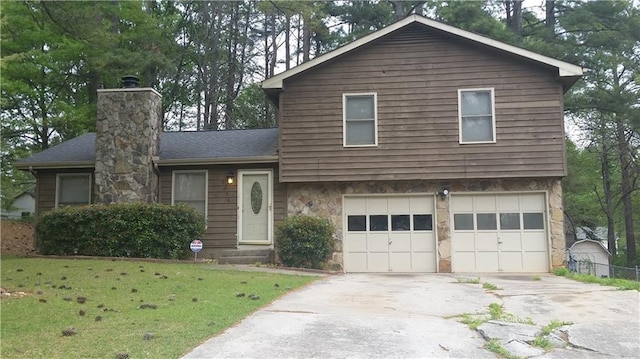 split level home featuring driveway, a shingled roof, a chimney, an attached garage, and a front yard