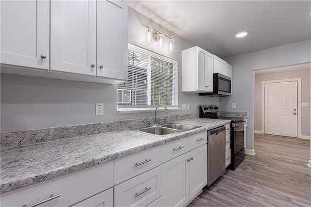 kitchen with white cabinetry, a sink, light wood-style floors, stainless steel appliances, and baseboards