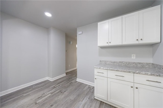 kitchen featuring light stone counters, white cabinetry, light wood-style floors, baseboards, and recessed lighting
