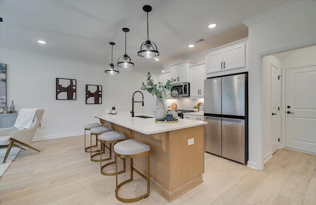 kitchen with a kitchen island with sink, white cabinets, sink, decorative light fixtures, and stainless steel appliances