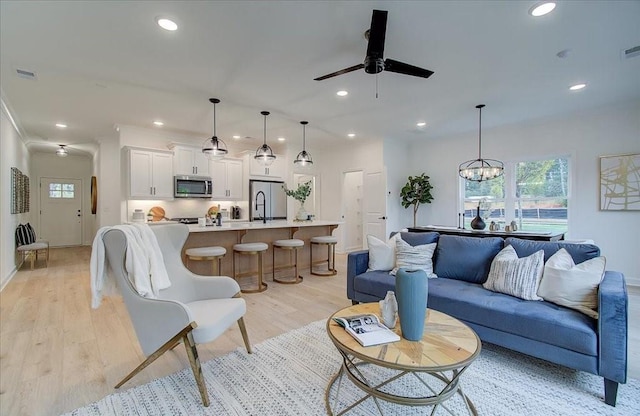 living room featuring sink, light hardwood / wood-style floors, and ceiling fan with notable chandelier