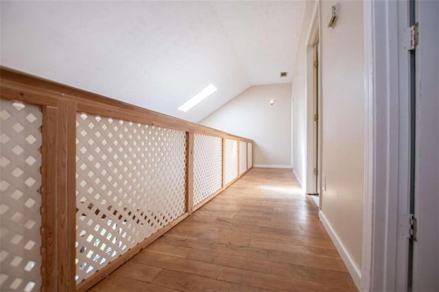 hallway with vaulted ceiling with skylight and light hardwood / wood-style floors