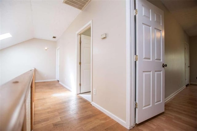 hallway featuring vaulted ceiling with skylight and light wood-type flooring