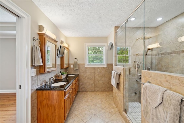 bathroom with a textured ceiling, tile walls, an enclosed shower, and vanity