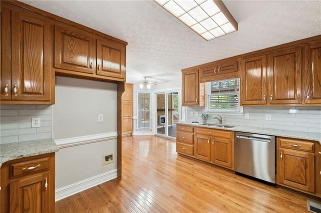 kitchen featuring tasteful backsplash, light stone countertops, stainless steel dishwasher, light hardwood / wood-style floors, and sink