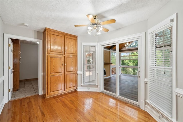 interior space with a textured ceiling, ceiling fan, and light hardwood / wood-style flooring