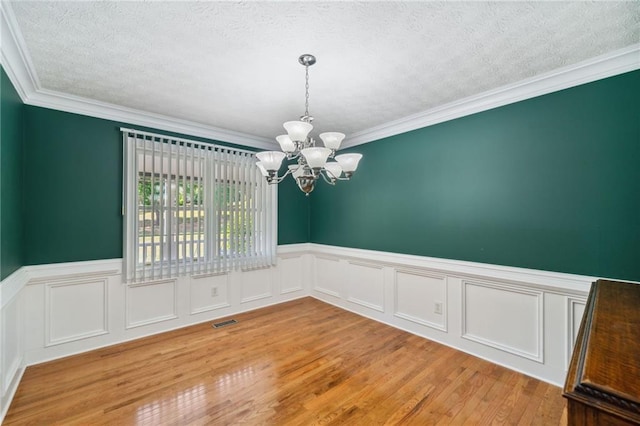 empty room with ornamental molding, light hardwood / wood-style flooring, a chandelier, and a textured ceiling