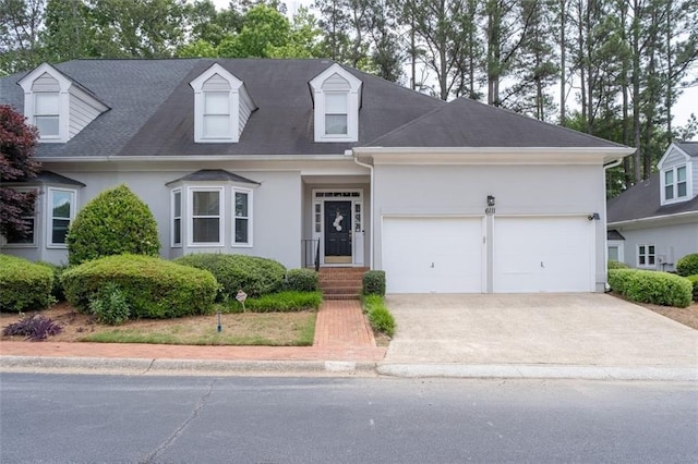new england style home featuring stucco siding, concrete driveway, an attached garage, and roof with shingles