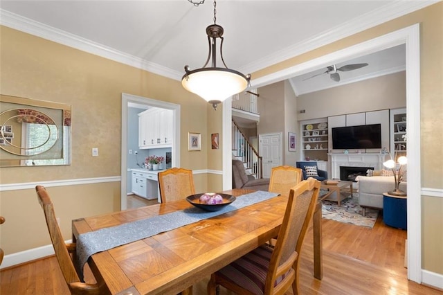dining room with stairway, light wood-style flooring, ornamental molding, a fireplace, and a ceiling fan