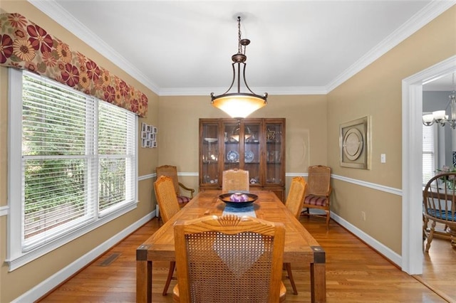 dining room featuring light wood-type flooring, ornamental molding, a chandelier, and baseboards