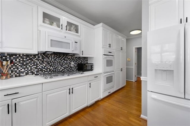 kitchen with white appliances, light countertops, backsplash, white cabinets, and light wood finished floors