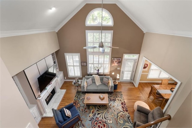 living area with a fireplace with flush hearth, wood finished floors, high vaulted ceiling, baseboards, and crown molding