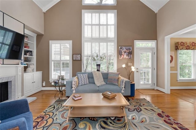 living room with crown molding, light wood-style floors, high vaulted ceiling, baseboards, and a premium fireplace