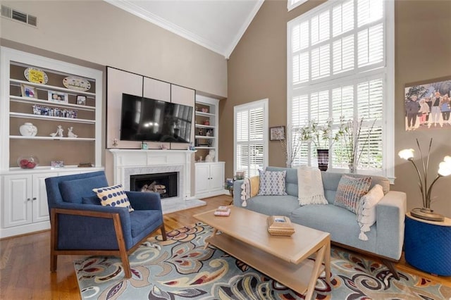 living room featuring crown molding, high vaulted ceiling, wood finished floors, a premium fireplace, and built in shelves
