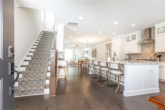 kitchen with visible vents, dark wood finished floors, an island with sink, wall chimney exhaust hood, and tasteful backsplash