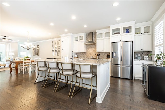 kitchen featuring a breakfast bar area, dark wood-style floors, a center island with sink, wall chimney range hood, and stainless steel fridge