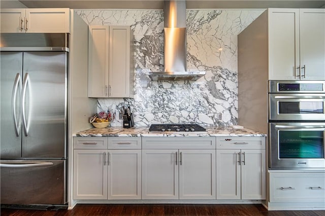 kitchen featuring light stone countertops, dark wood-type flooring, stainless steel appliances, tasteful backsplash, and wall chimney exhaust hood