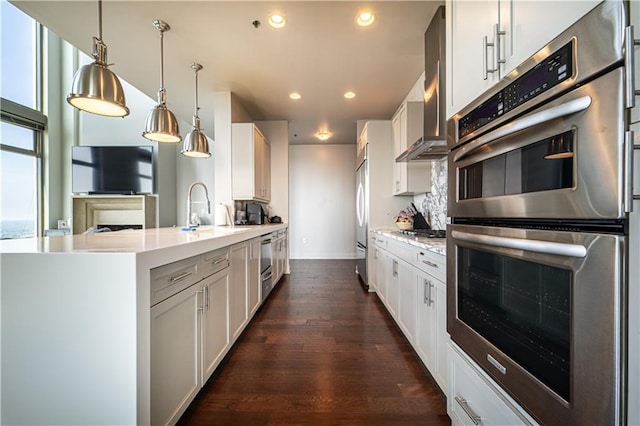 kitchen featuring hanging light fixtures, white cabinets, stainless steel appliances, dark wood-type flooring, and wall chimney exhaust hood