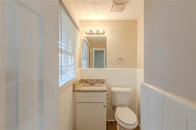 bathroom with vanity, toilet, tile walls, and a textured ceiling