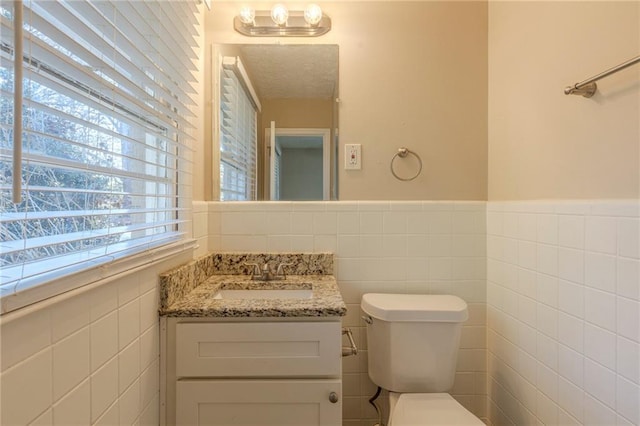 bathroom featuring toilet, vanity, and tile walls