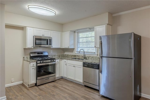 kitchen featuring light stone countertops, appliances with stainless steel finishes, white cabinetry, sink, and light wood-type flooring