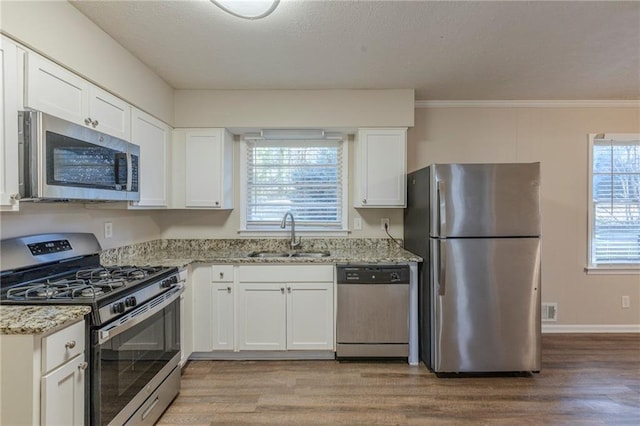 kitchen featuring appliances with stainless steel finishes, sink, plenty of natural light, white cabinetry, and light stone countertops