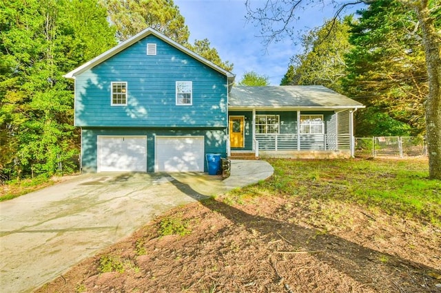 tri-level home with a porch, fence, an attached garage, and driveway