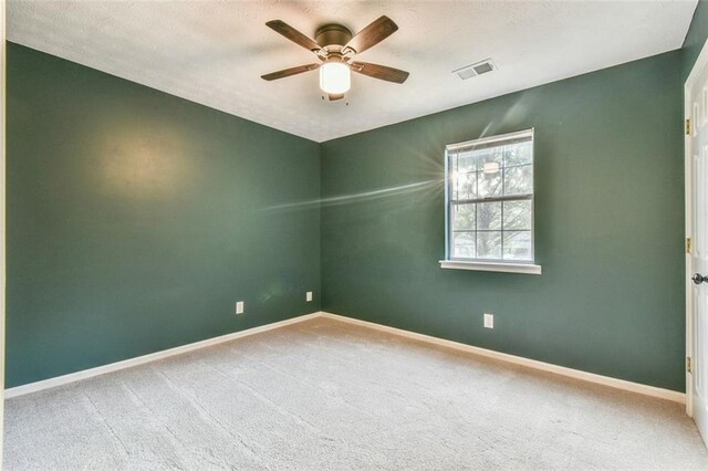 spare room featuring carpet floors, visible vents, baseboards, and ceiling fan