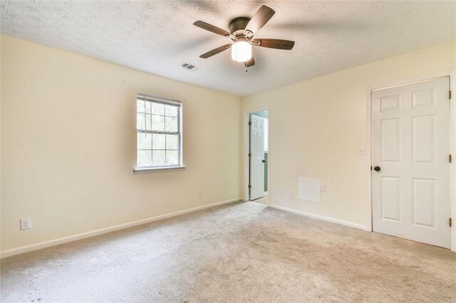 carpeted empty room with a textured ceiling, baseboards, a ceiling fan, and visible vents