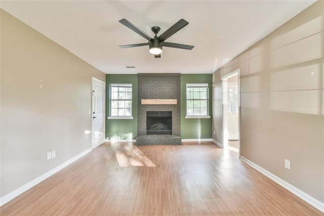 unfurnished living room featuring ceiling fan, visible vents, wood finished floors, a brick fireplace, and baseboards