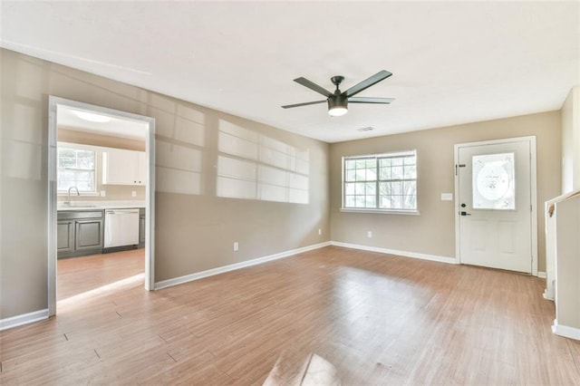 unfurnished living room featuring light wood-style flooring, a sink, a ceiling fan, and a healthy amount of sunlight