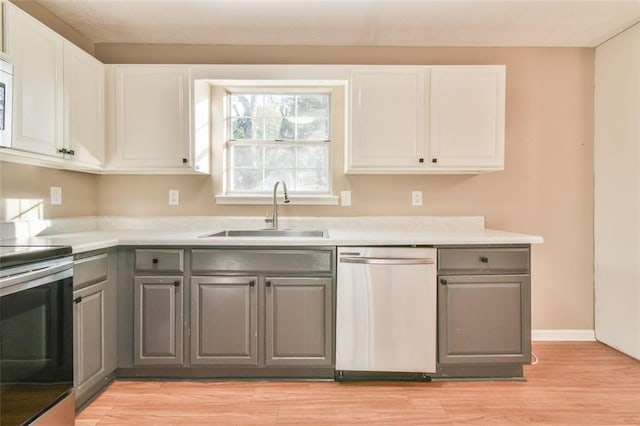 kitchen featuring light wood-type flooring, gray cabinets, white cabinetry, appliances with stainless steel finishes, and a sink