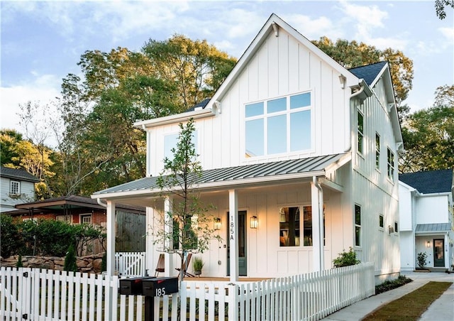 modern inspired farmhouse with a standing seam roof, a porch, a fenced front yard, board and batten siding, and metal roof