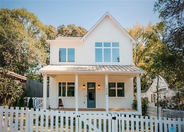 modern inspired farmhouse with a standing seam roof, a fenced front yard, board and batten siding, covered porch, and metal roof