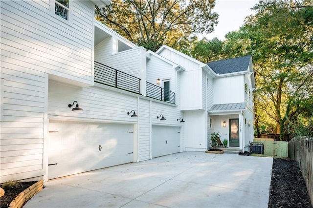 back of house with fence, board and batten siding, concrete driveway, a garage, and a balcony