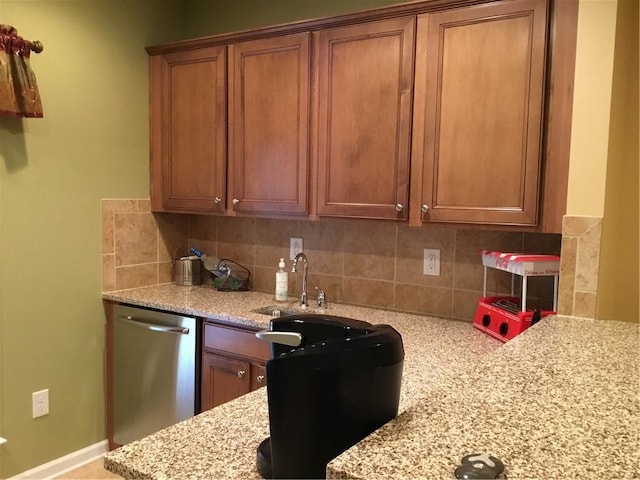 kitchen with light stone counters, brown cabinets, tasteful backsplash, stainless steel dishwasher, and a sink