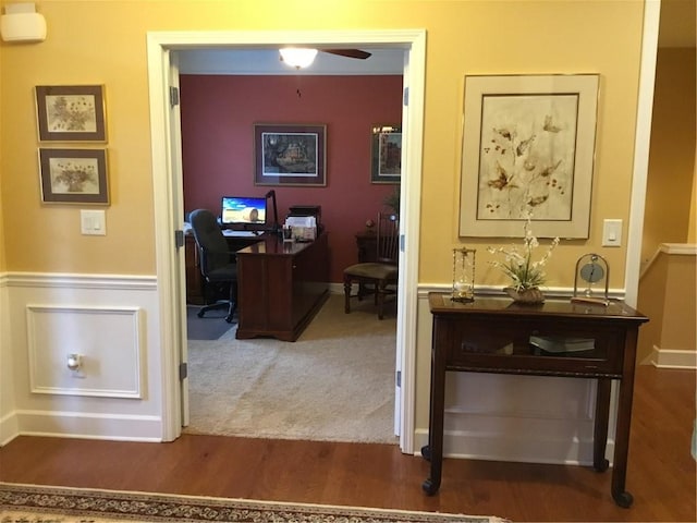 carpeted office with wainscoting, ceiling fan, and wood finished floors