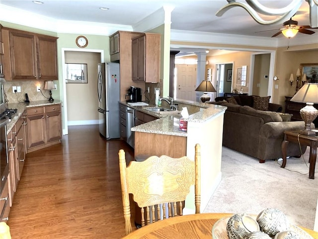 kitchen featuring appliances with stainless steel finishes, open floor plan, a sink, a peninsula, and ornate columns