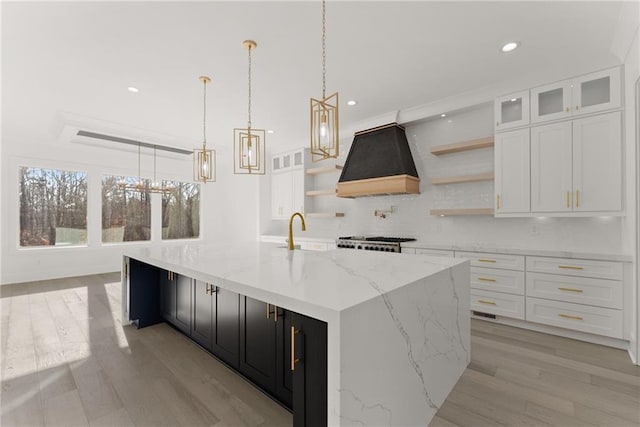 kitchen featuring hanging light fixtures, tasteful backsplash, white cabinets, custom exhaust hood, and a large island with sink